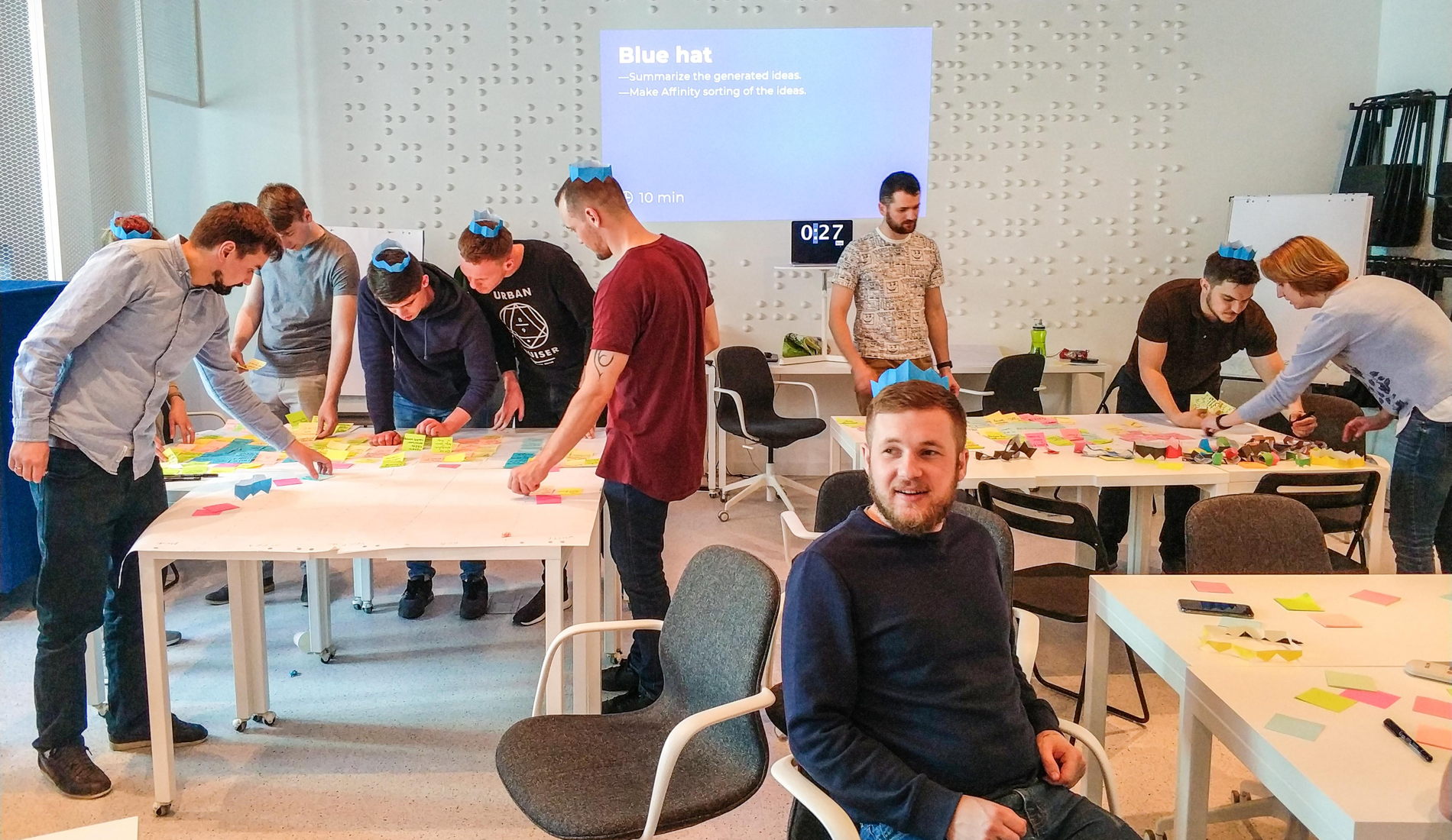 Group workshop in a bright room; people collaborate at tables with papers and sticky notes.